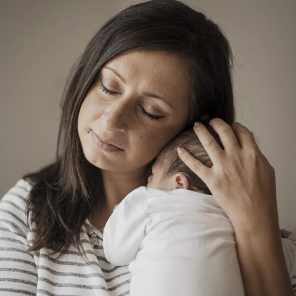 Mãe de olhos fechados, segurando e acolhendo seu bebê recém-nascido com ternura, transmitindo amor e vínculo no período pós-parto.